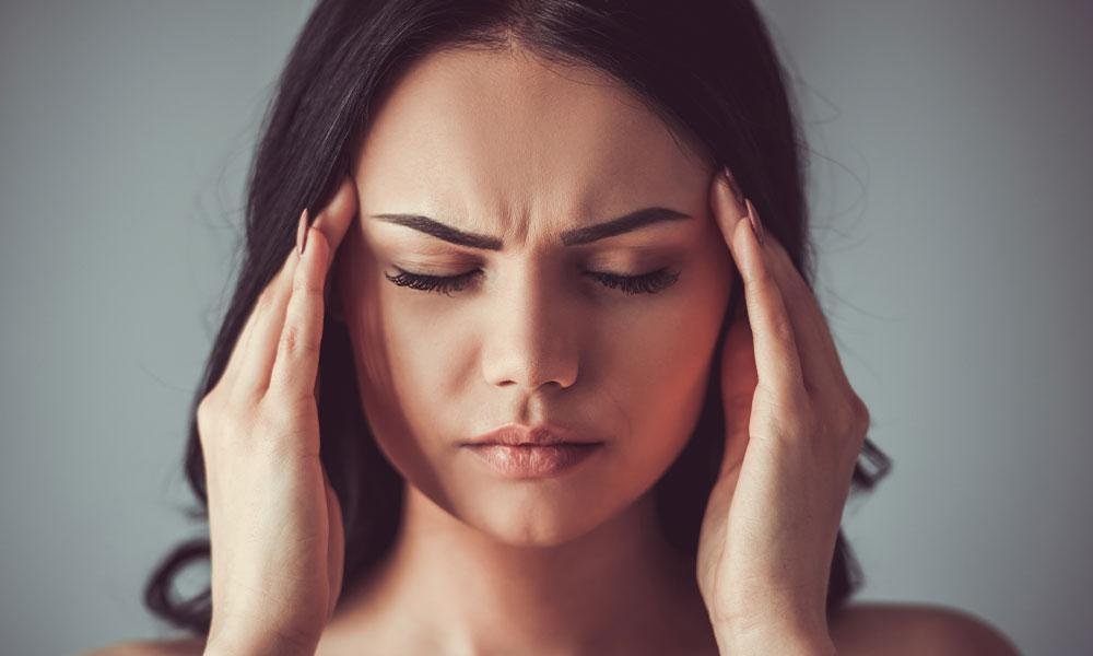 Woman holding head in pain in a dark room